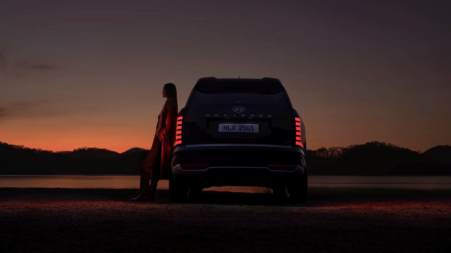 2026-hyundai-palisade-back-view-at-sunset-with-woman-leaning-on-car