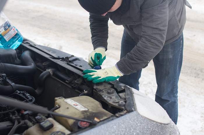 Man repairing car in winter, under hood
