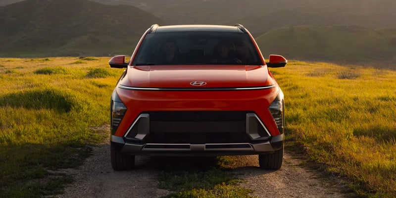 Red Hyundai Kona SUV front view parked on a scenic grassy landscape.