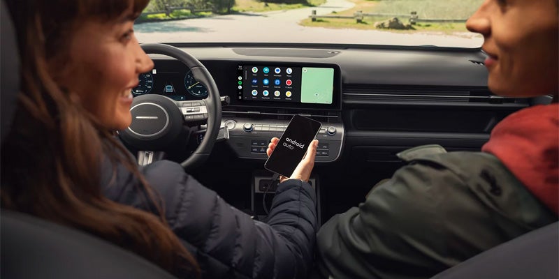 Hyundai Kona interior with passengers using the touchscreen infotainment system and smartphone connectivity features.
