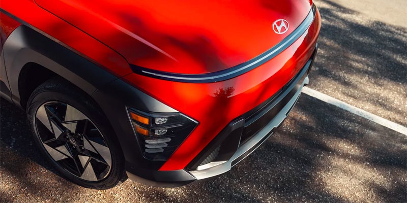 Red Hyundai Kona exterior detail showing the front grille, headlight design, and alloy wheel.