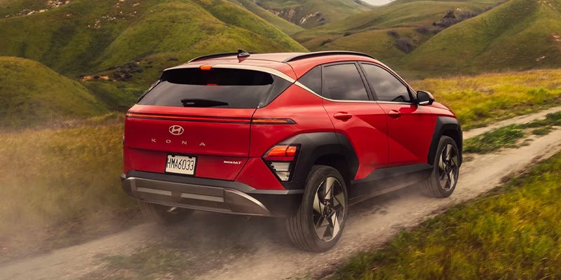 Red Hyundai Kona SUV driving on a dusty mountain road with rugged terrain.