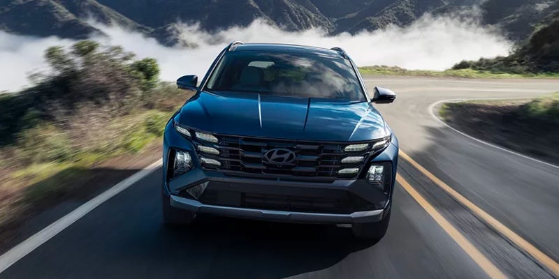 Hyundai Tucson driving on a winding road with mountains in the background.