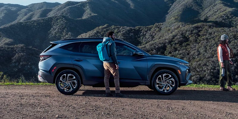 Blue Hyundai Tucson SUV parked near a mountain landscape with a person exploring outdoors.