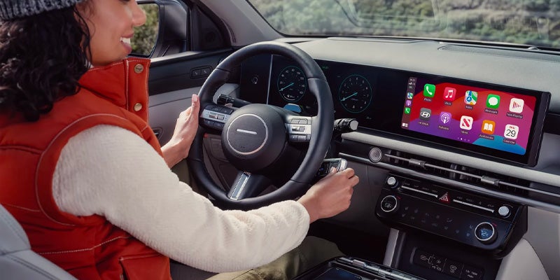 Hyundai Tucson interior with driver using touchscreen infotainment and steering wheel controls.