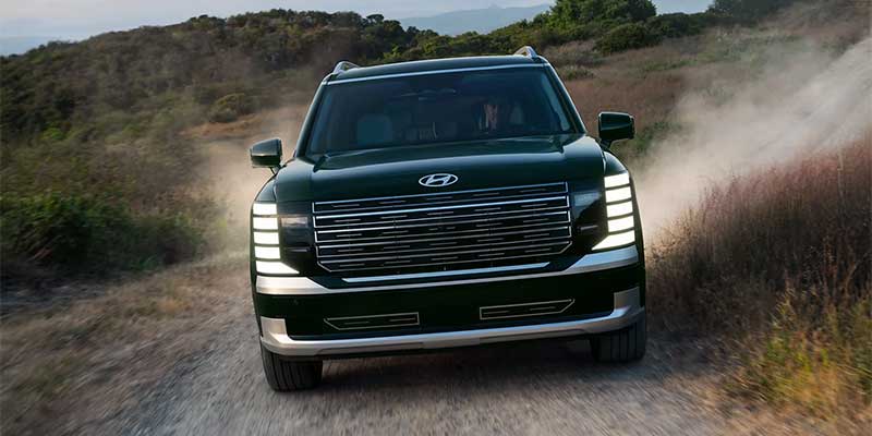 Hyundai Palisade driving on a dusty off-road trail with rugged terrain in the background.