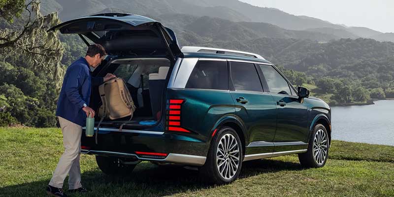 Hyundai Palisade with rear liftgate open and cargo area being loaded near a scenic mountain landscape.