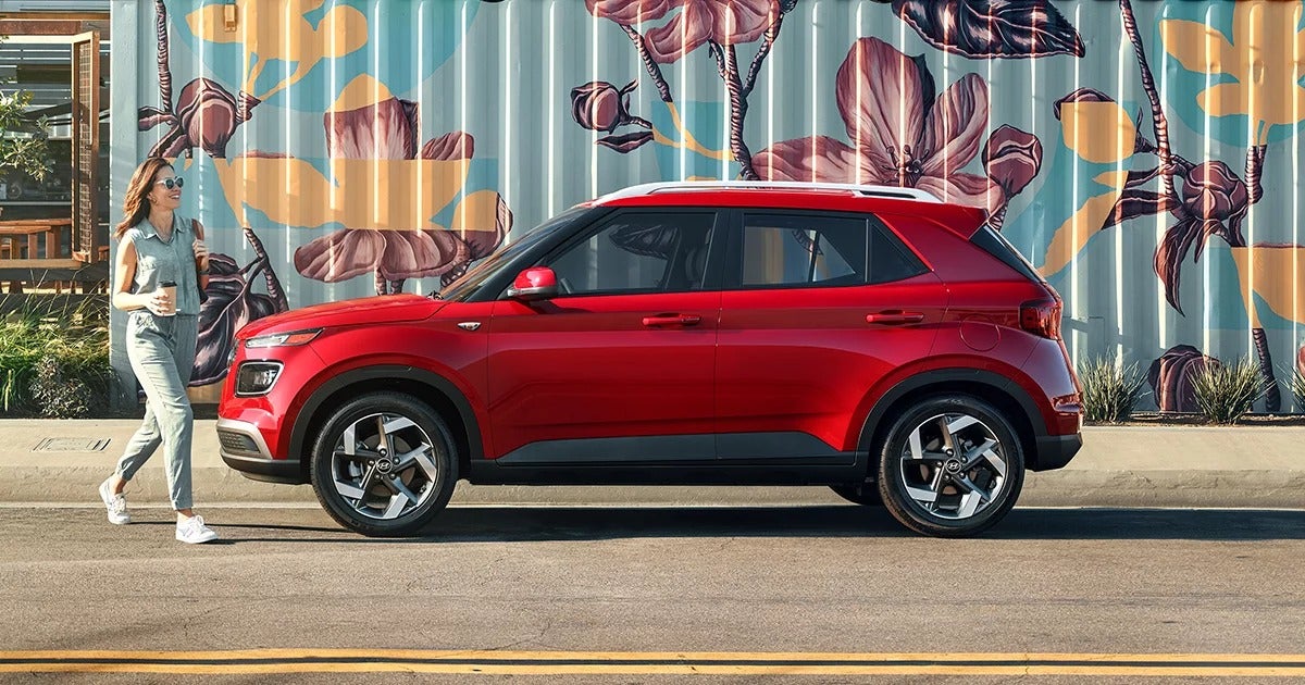 Red Hyundai Venue parked in front of a vibrant floral mural, with a woman walking nearby holding a coffee cup.