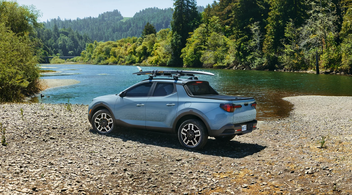 Light blue Hyundai Santa Cruz by a river with surfboard on roof at Windward Hyundai Kaneohe HI.