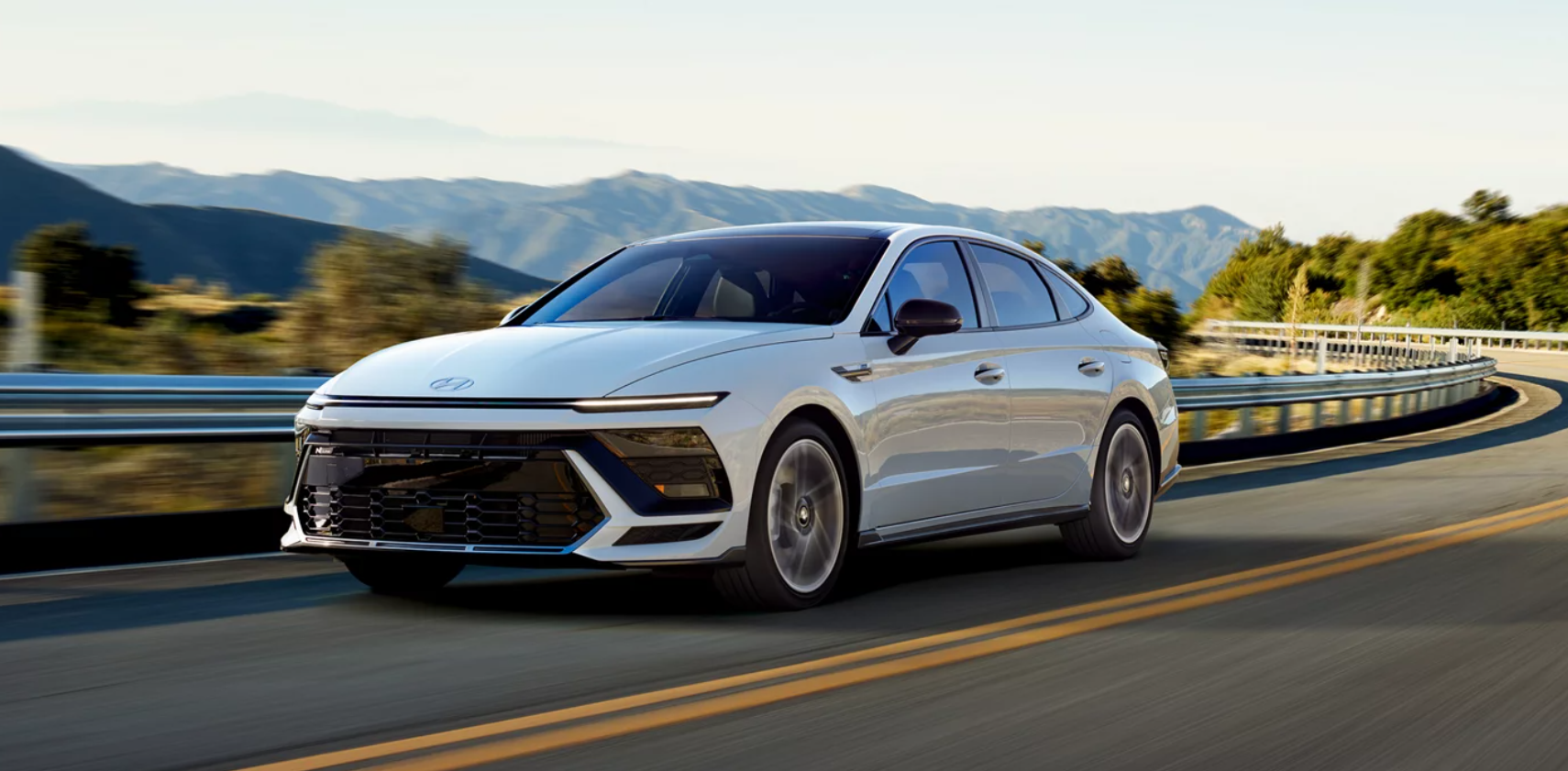 2026 Hyundai Sonata Hybrid driving fast on highway next to mountains.
